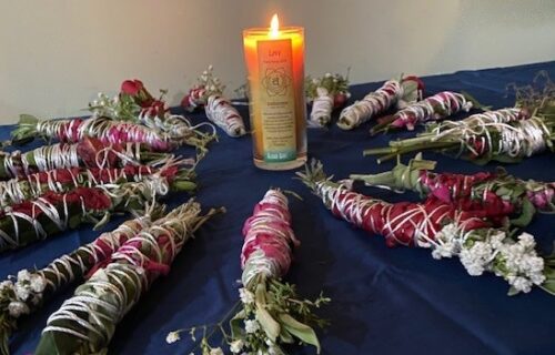 Image of sage bundles surrounding a candle on a table.